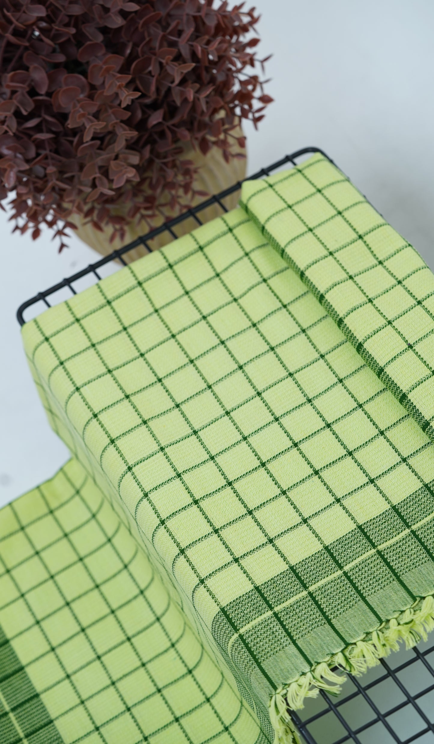 Chennimalai Soft Grid Weave Towel Lime Green on a table with a plant in the background