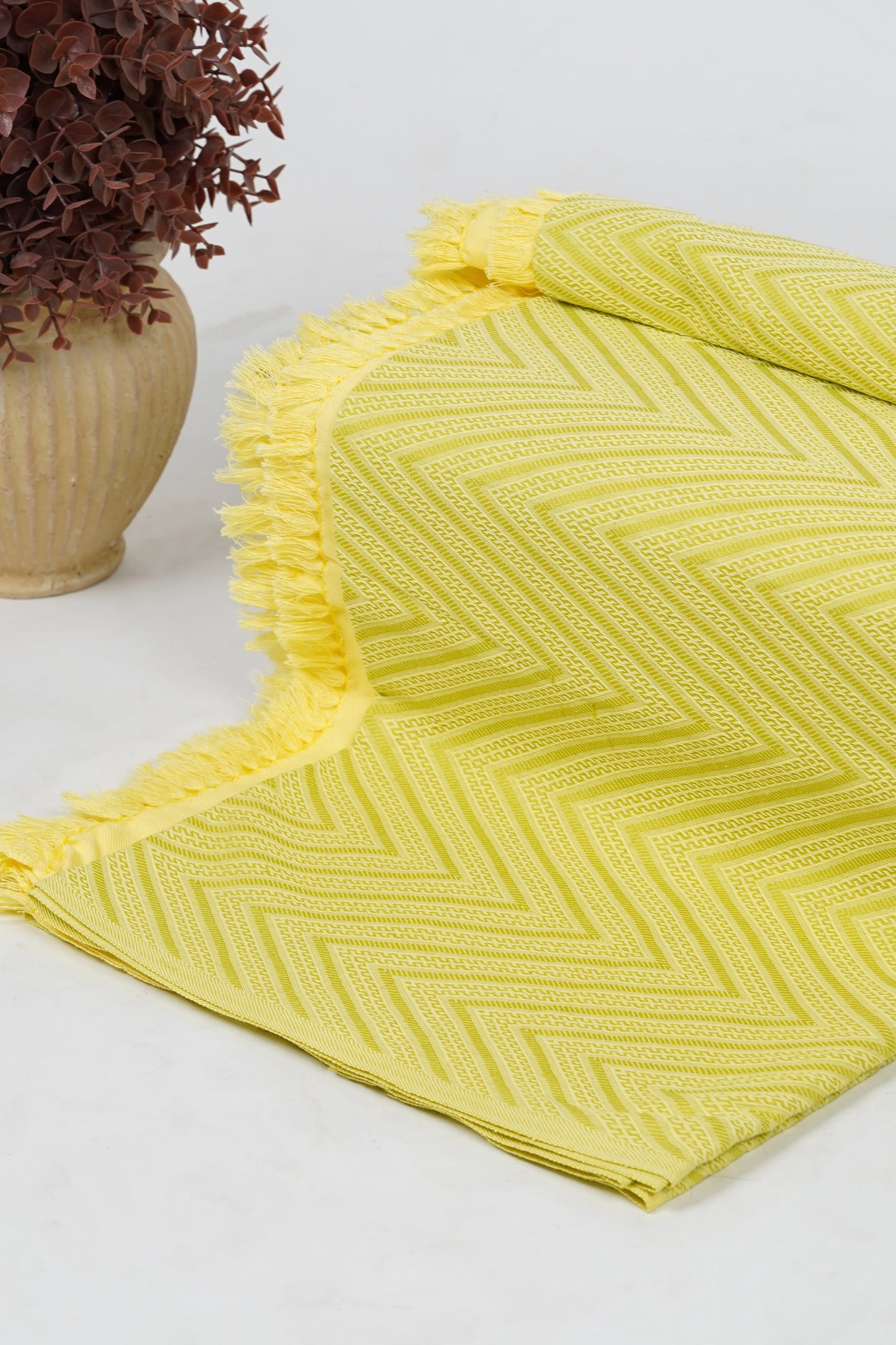 Yellow textured blanket on a white surface with a vase of dried flowers.