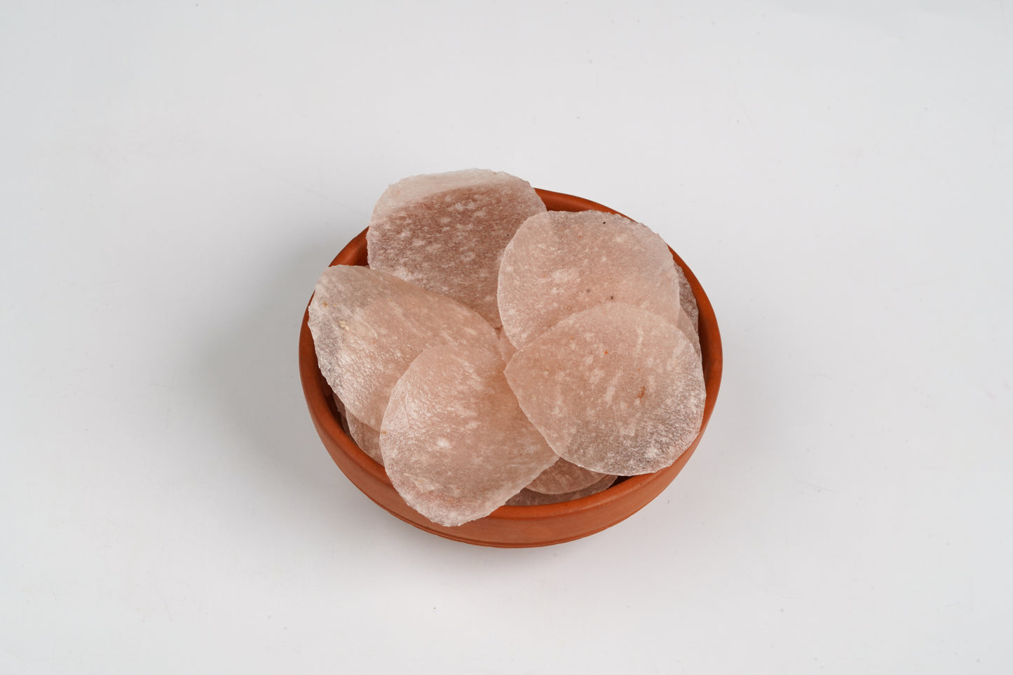 Round brown soap bars in a wooden bowl on a light gray background