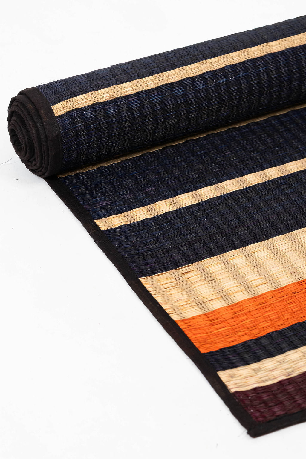 Rolled-up striped rug with black, orange, and beige pattern on a white background