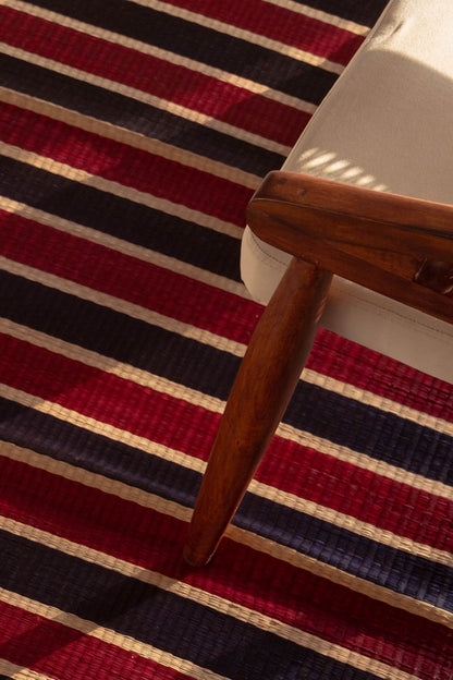 Close-up of a chair with wooden armrest on a striped red, black, and beige rug.