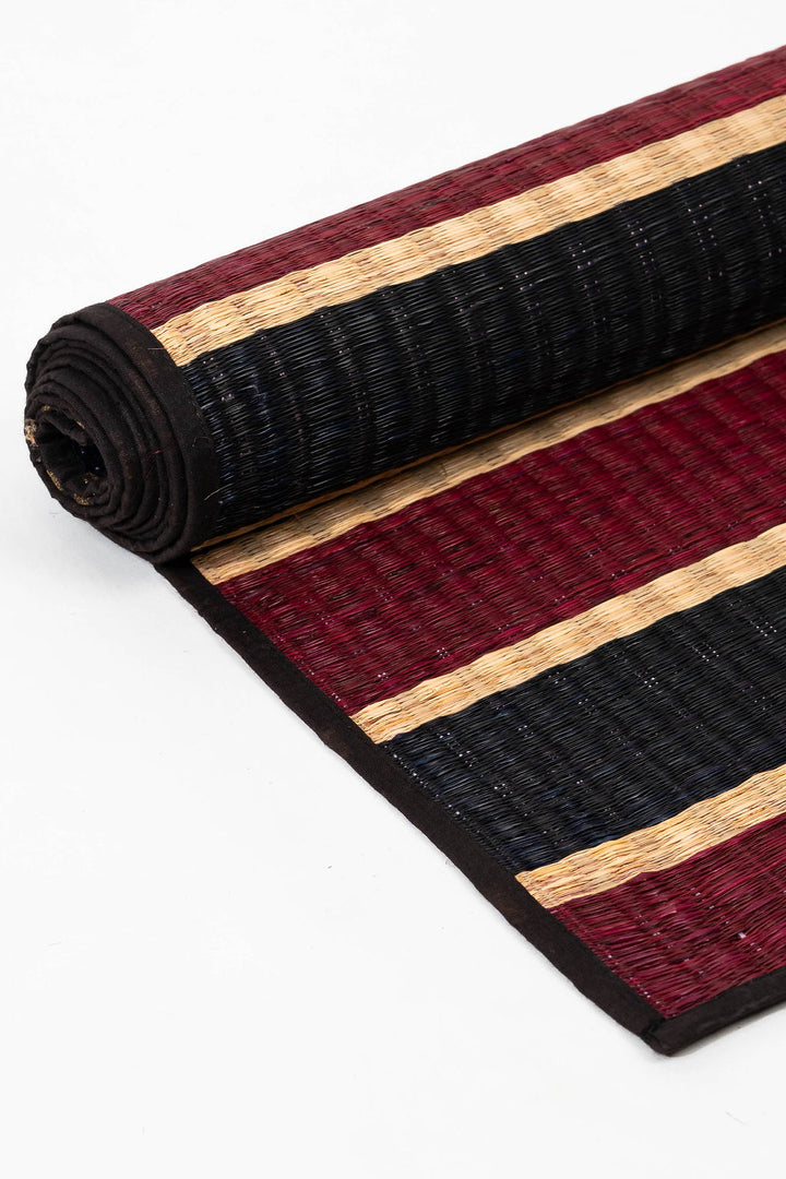 Rolled-up striped grass mat with red, black, and beige pattern on a white background
