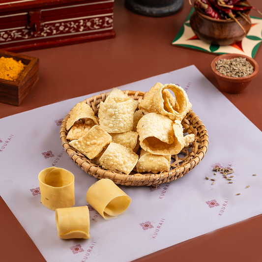 A basket filled with crispy, flower-shaped Appalam wafers on a table, with spices scattered around.