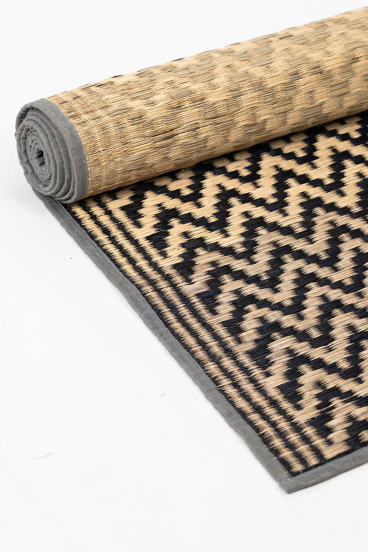 Rolled-up geometric patterned rug with natural and gray border on a white background