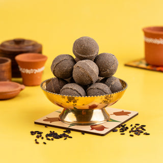A bowl of black rice ghee ladoo (Karuppu Kavuni) on a yellow background, with decorative elements around it.