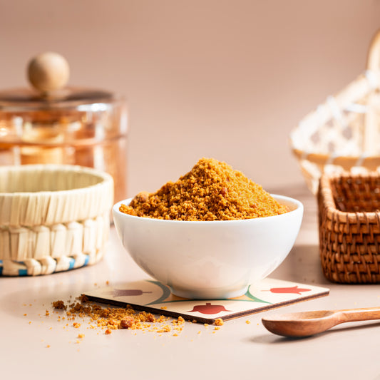 A bowl of brown sugar is placed on a table with a wooden spoon beside it. In the background, there are containers and a basket, creating a cozy kitchen atmosphere.
