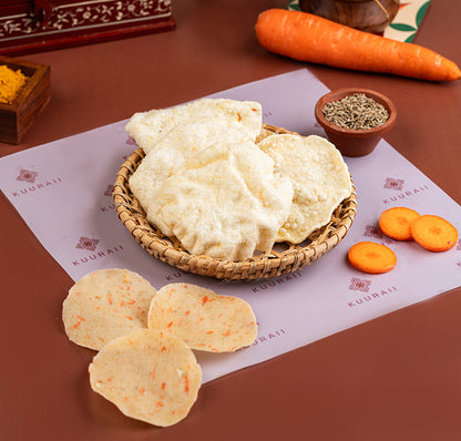 A plate of Carrot Vadagam, which are round, flat snacks made from sun-dried carrots, displayed alongside whole carrots and spices.