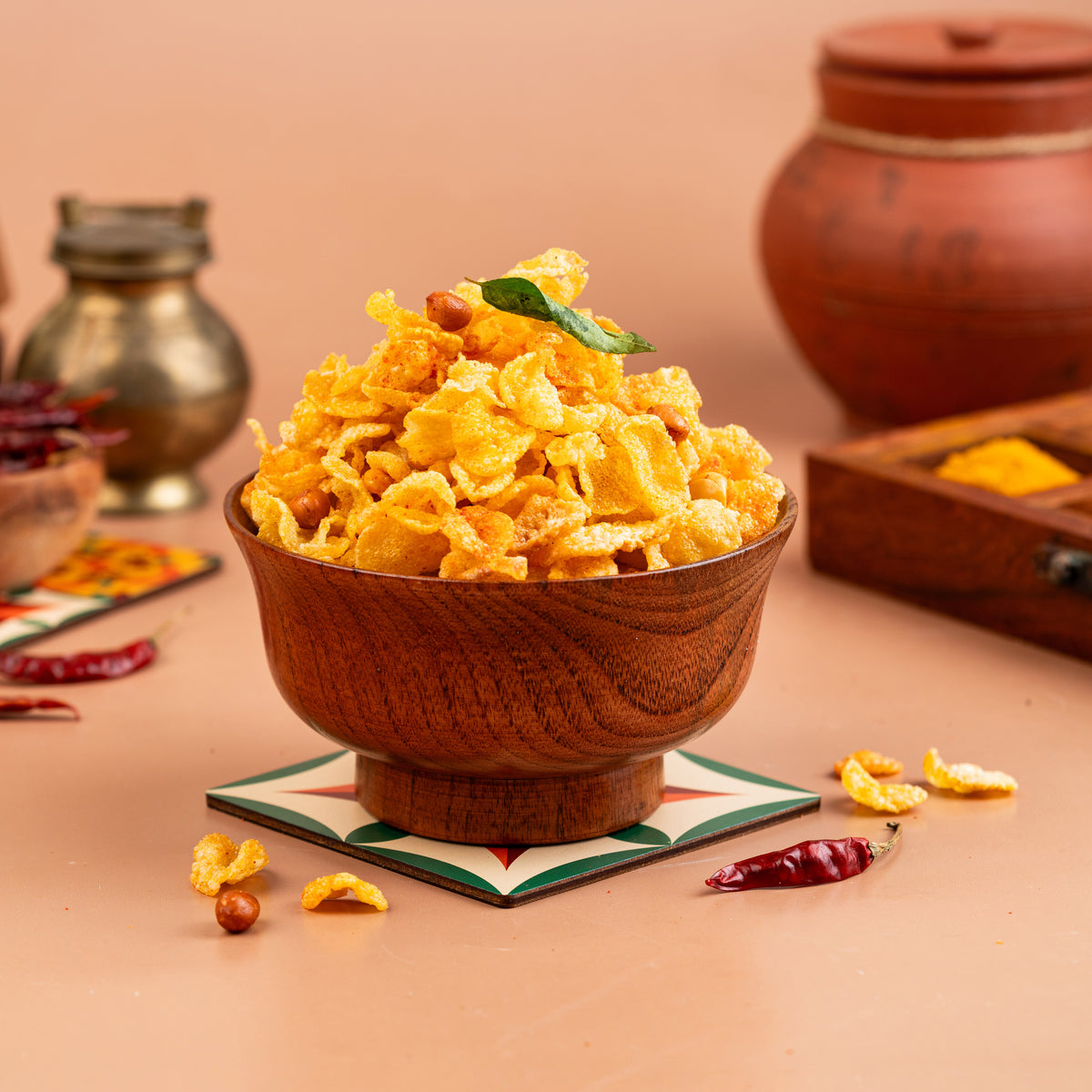 A wooden bowl filled with fried corn mixture, garnished with a leaf, on a placemat with spices and a condiment bowl in the background.