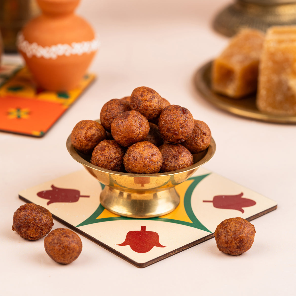 A bowl of Chettinad Inipu Seedai (Sweet Seedai) placed on a colorful patterned plate, with more seedai visible outside the bowl. The background includes a vase with flowers and some traditional sweets.