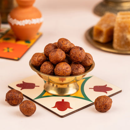 A bowl of Chettinad Inipu Seedai (Sweet Seedai) placed on a colorful patterned plate, with more seedai visible outside the bowl. The background includes a vase with flowers and some traditional sweets.
