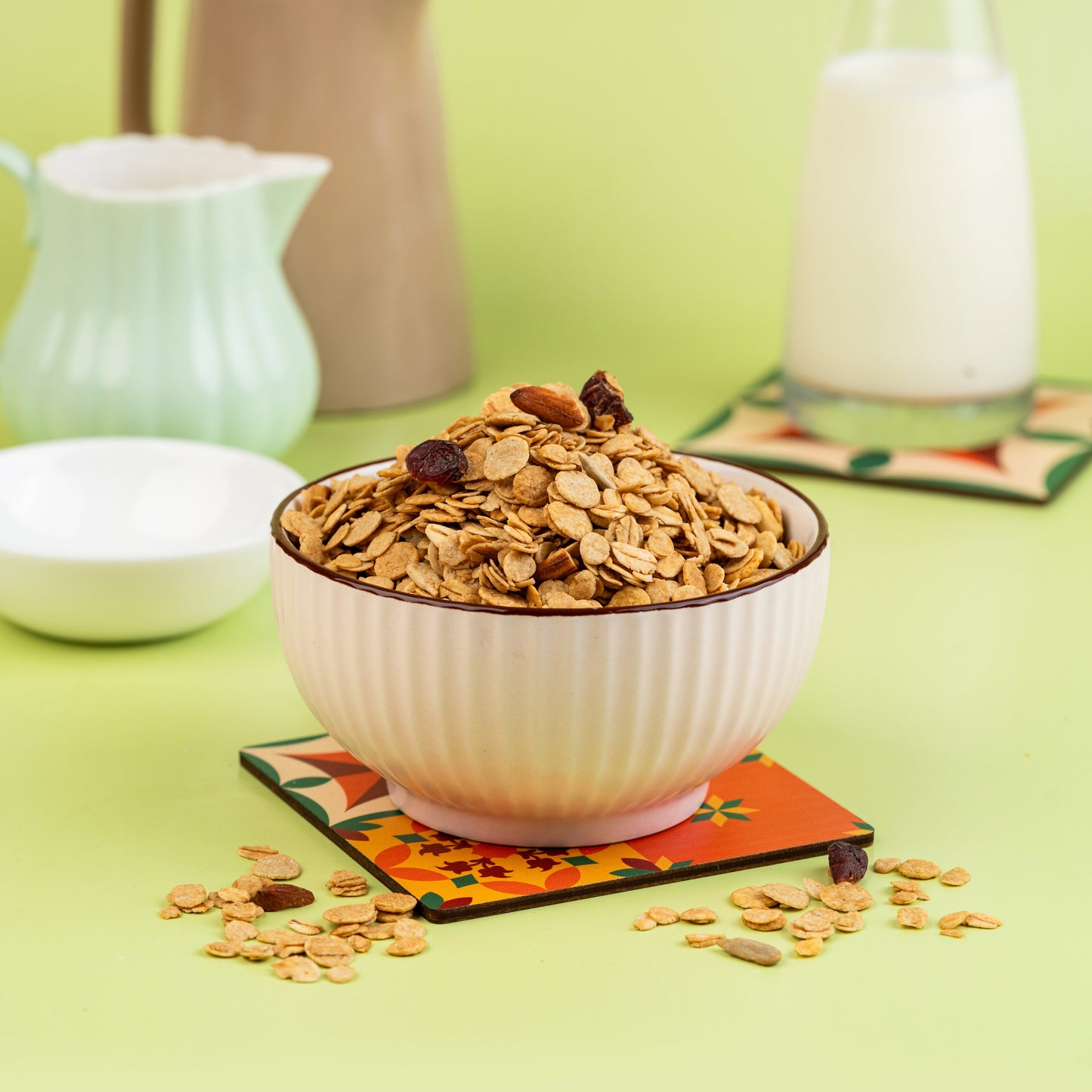 A bowl of classic muesli made of crunchy oats, nuts, and dried fruits, placed on a colorful coaster with a bottle of milk and a cream-colored bowl in the background.