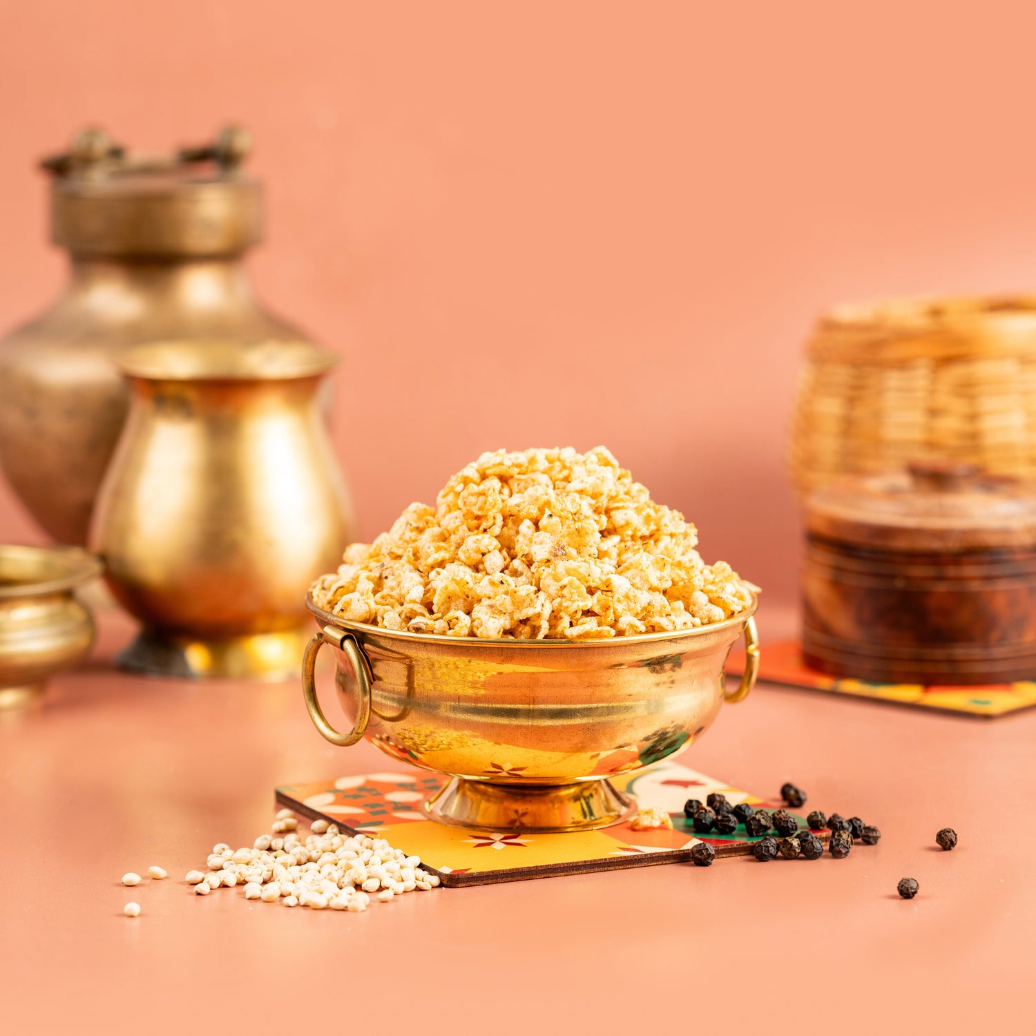 A bowl of air fried cholam (millet) spicy snacks on a table with a golden background, accompanied by spices and more traditional snacks.