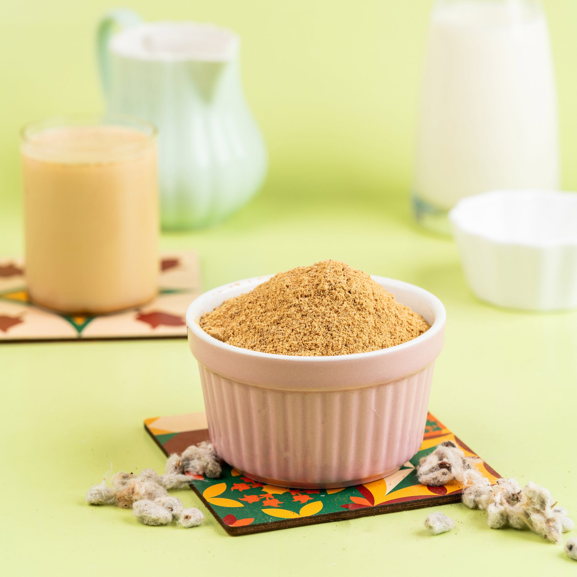 A bowl of cotton seed milk (Paruthi Paal) served on a colorful mat, with a glass and cotton flowers in the background.