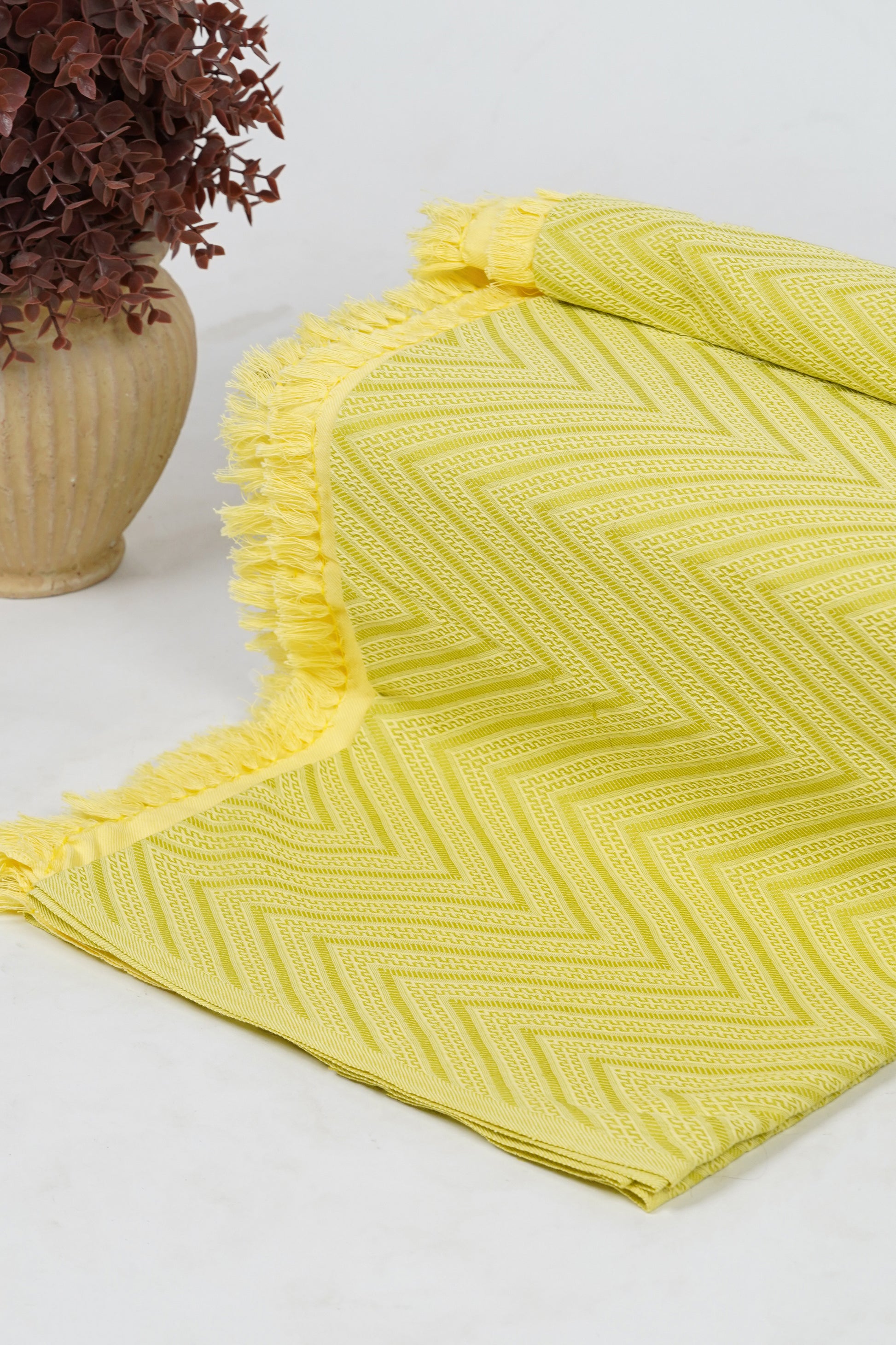 Yellow textured blanket on a white surface with a vase of dried flowers.