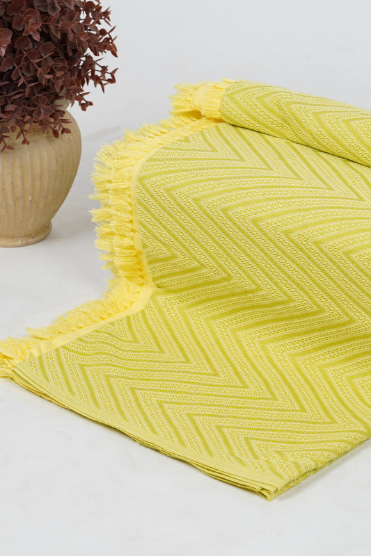 Yellow textured blanket on a white surface with a vase of dried flowers.