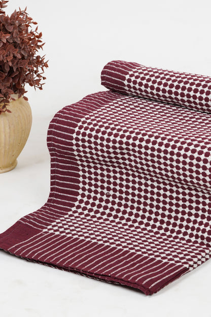 Folded patterned fabric on a white surface with a vase of dried flowers.