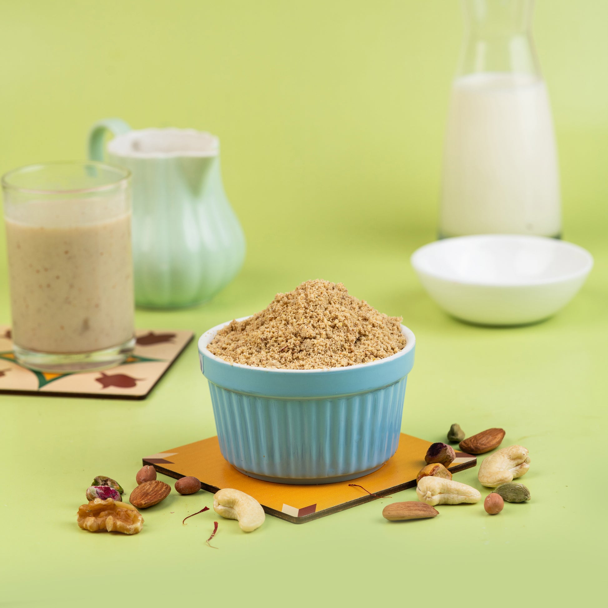 A bowl of Dry Nuts Powder with Palm Candy on a green mat, with a glass of milk and pieces of nuts and palm candy in the background.