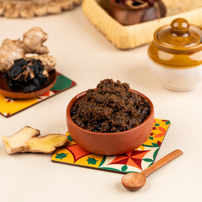 A bowl of Ginger-Tamarind Thokku (Inji Puli) served on a colorful patterned mat alongside ingredients like tamarind and ginger, with a wooden spoon.