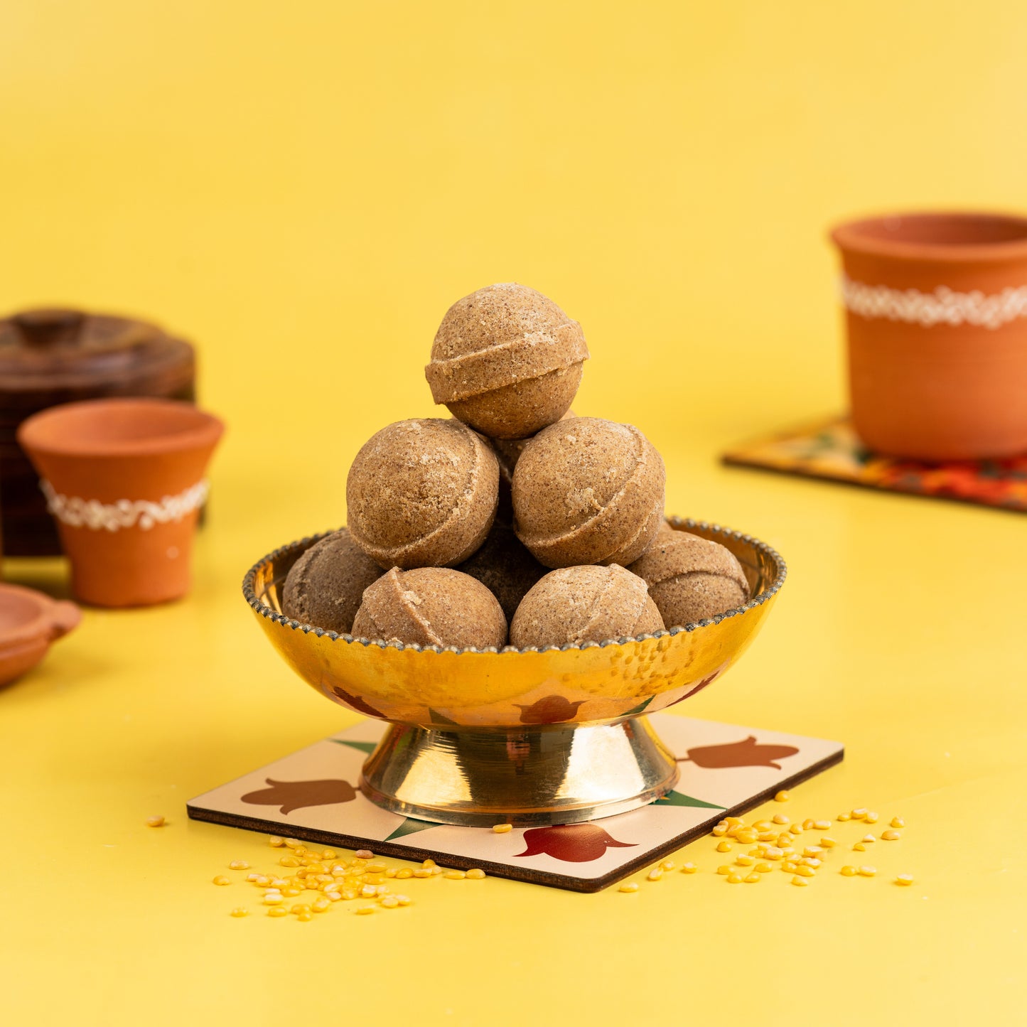 A traditional Indian sweet, Ghee Ladoo, made from green gram (millet), presented in a decorative bowl, with cultural elements in the background.