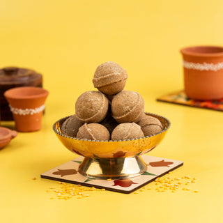 A traditional Indian sweet, Ghee Ladoo, made from green gram (millet), presented in a decorative bowl, with cultural elements in the background.