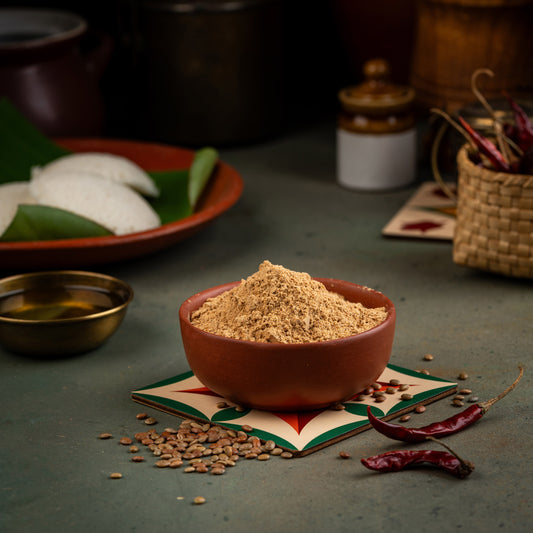 A bowl of Horse Gram Podi (Kollu) on a table with spices, herbs, and a woven basket in the background.