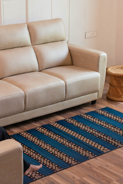 Beige sofa in a room with a blue patterned grass mat on the floor.