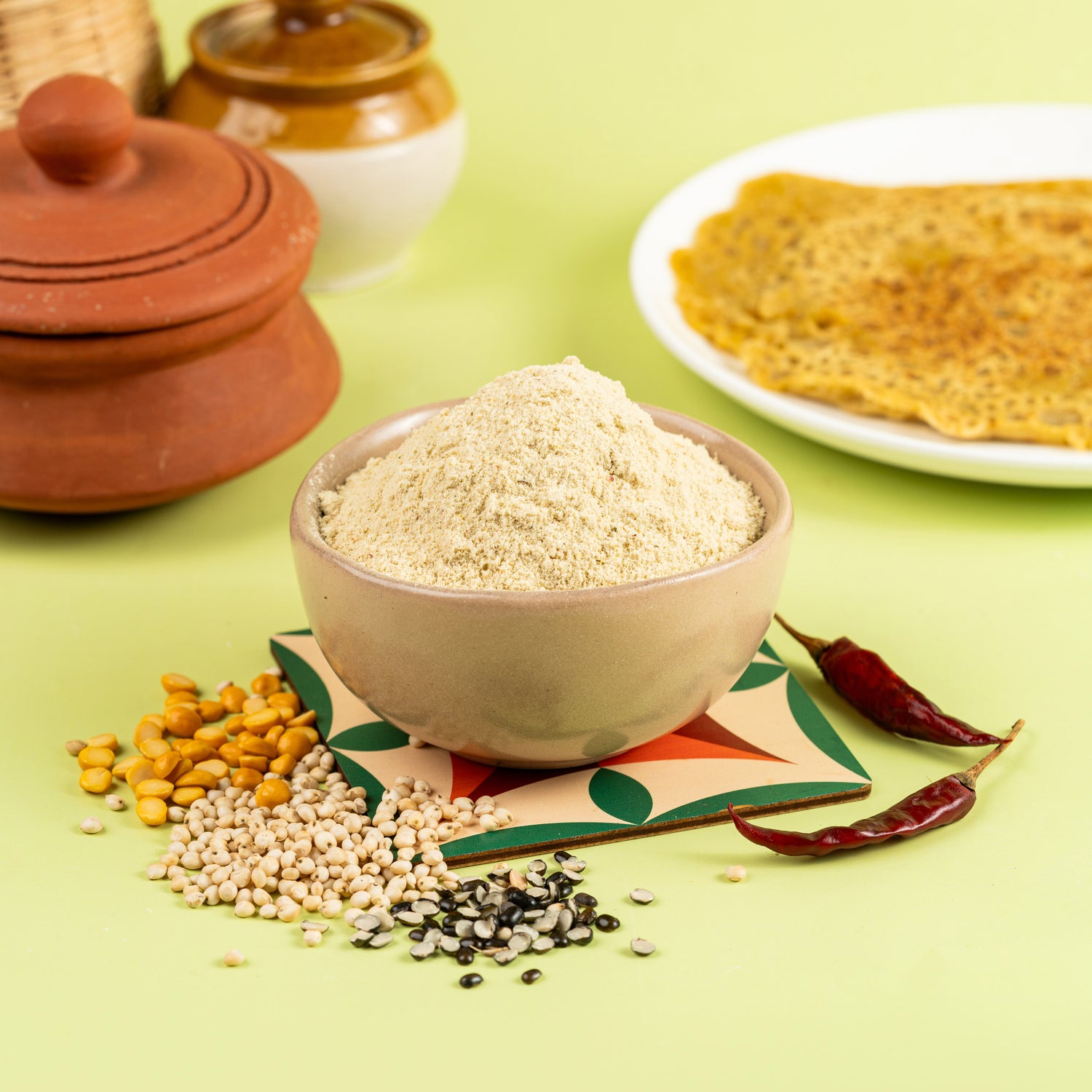 A bowl of Instant Adai Dosa Mix with millet, chickpeas, and spices displayed alongside, and a plate with a dosa on it in the background.