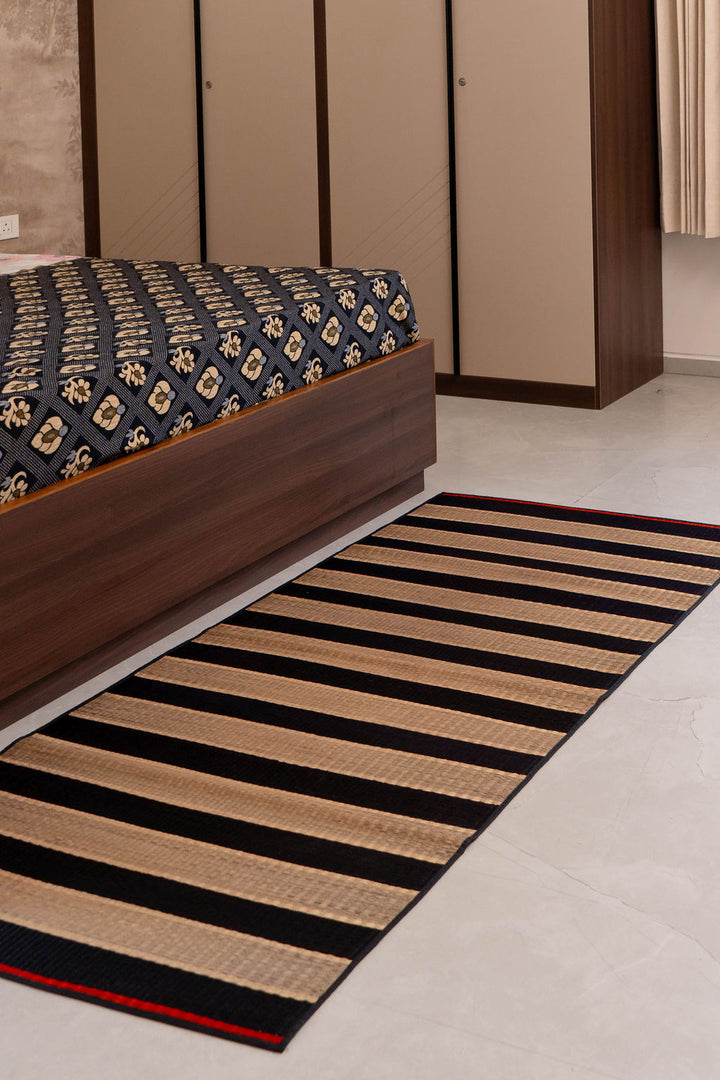 Striped rug on a floor next to a bed with a patterned bedspread.