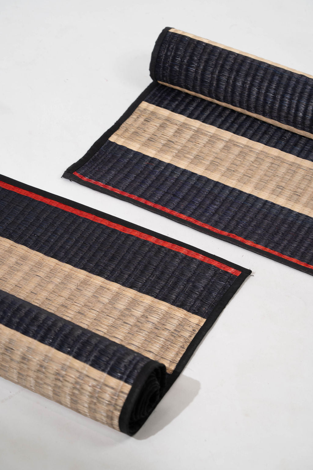 Two rolled-up mats with black and beige stripes on a white background
