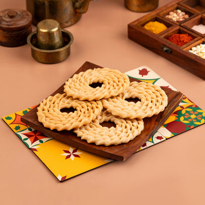 A plate with five circular murukkus, a traditional Indian snack, arranged on a wooden board with a colorful patterned napkin underneath.