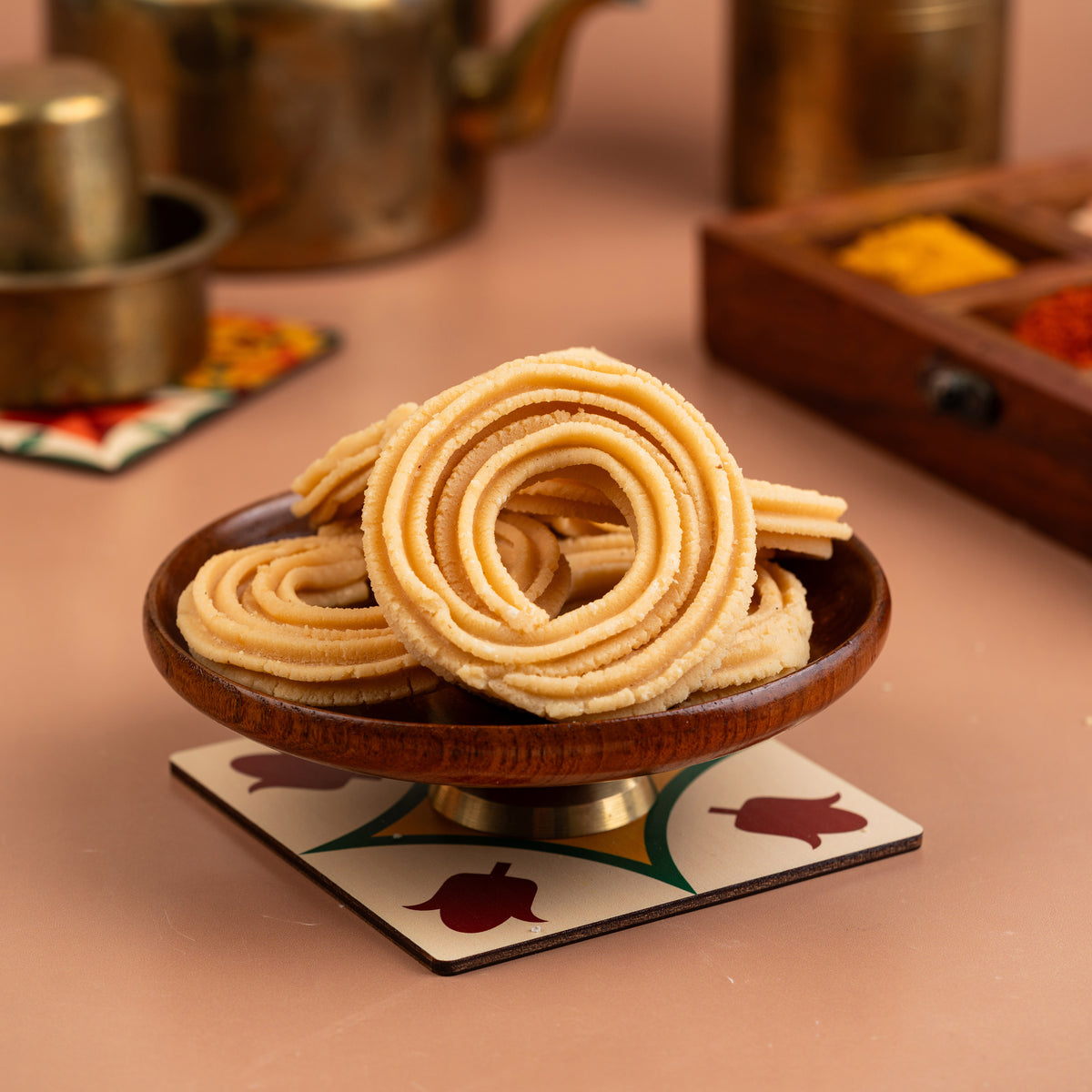 A plate of golden-brown Karaikudi Pirandai Murukku (Veldt Grape Murukku) served on a decorative coaster with a backdrop suggesting a traditional setting.