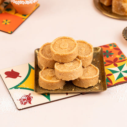 A plate of traditional Indian sweets, Thengai mittai, on a decorative paper plate with floral patterns.