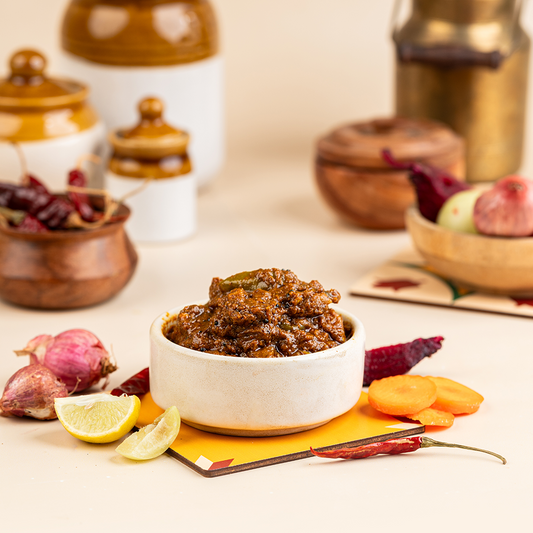 A bowl of Kathamba Pickle served alongside sliced vegetables and a lemon wedge, with ceramic jars in the background.