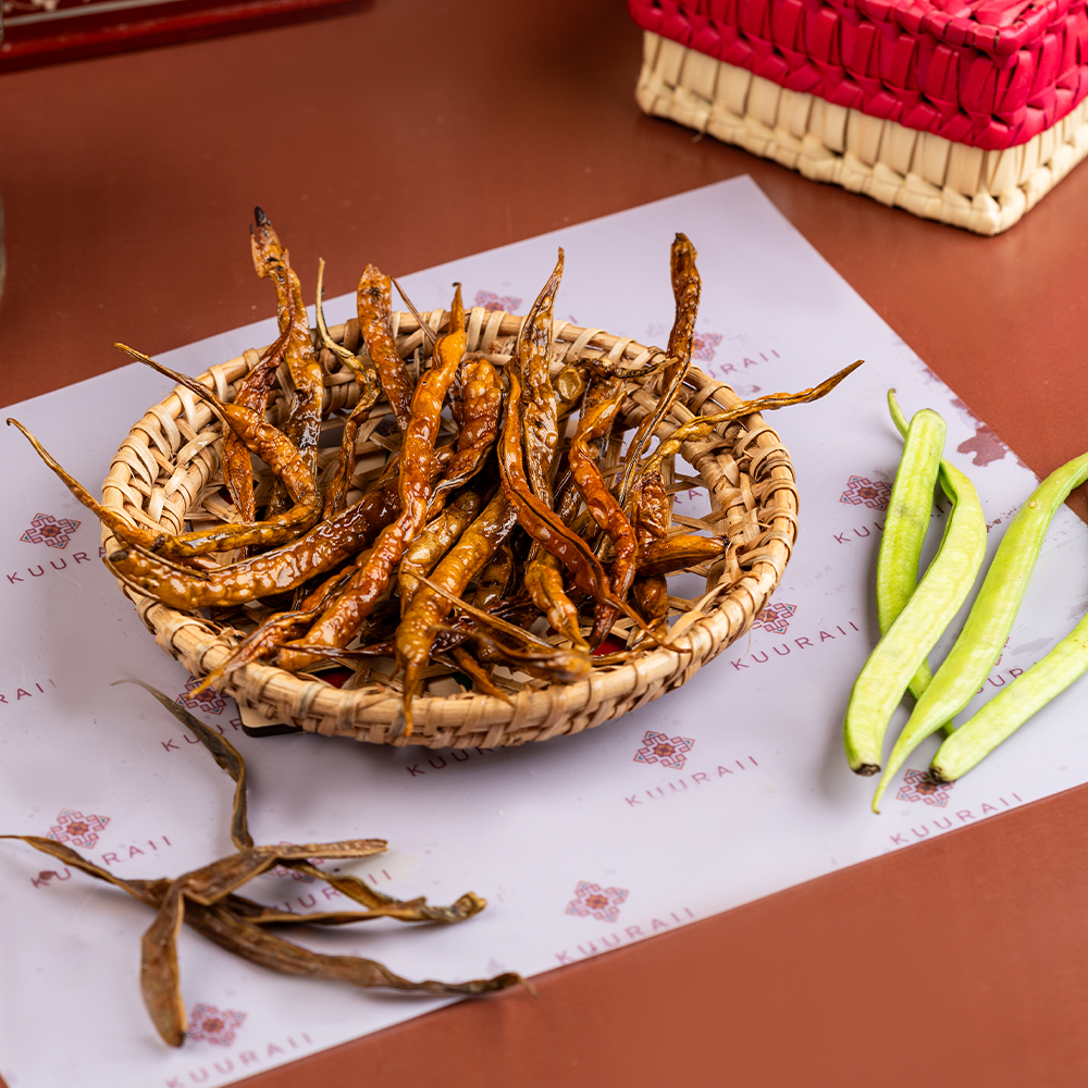 A basket filled with Kotthavarai Vathal, which are crispy sun-dried cluster beans, accompanied by fresh green cluster beans on the side.