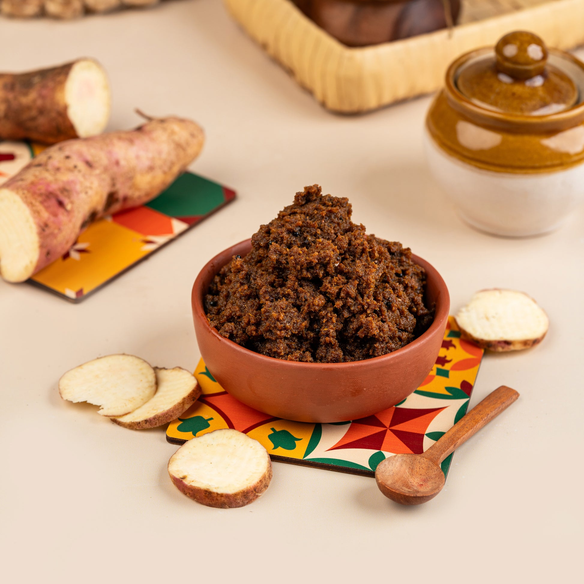 A bowl of Magaani Kizhangu Thokku with slices of cassava on the side, served on a colorful mat.