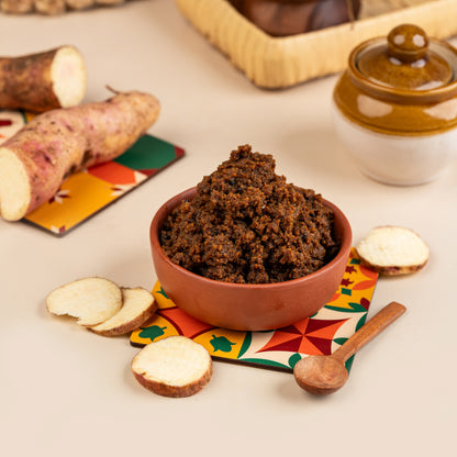 A bowl of Magaani Kizhangu Thokku with slices of cassava on the side, served on a colorful mat.