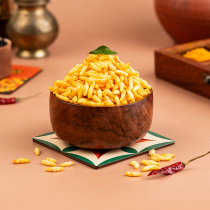 A wooden bowl filled with yellow masala puffed rice, placed on a colorful coaster with a decorative background.