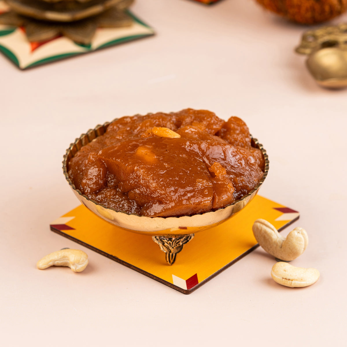 A brass bowl with a golden rim containing a sweet, thick, and syrupy halwa, with peanuts and dried fruits on the side.