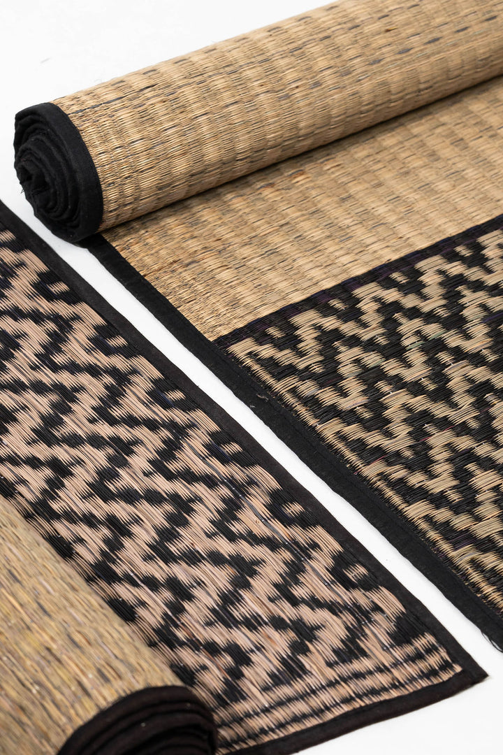 Rolled-up natural fiber grass mat with geometric pattern on a white background