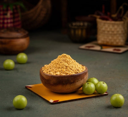 Wooden bowl filled with Nellikai Podi on a dark surface with Amla fruits around
