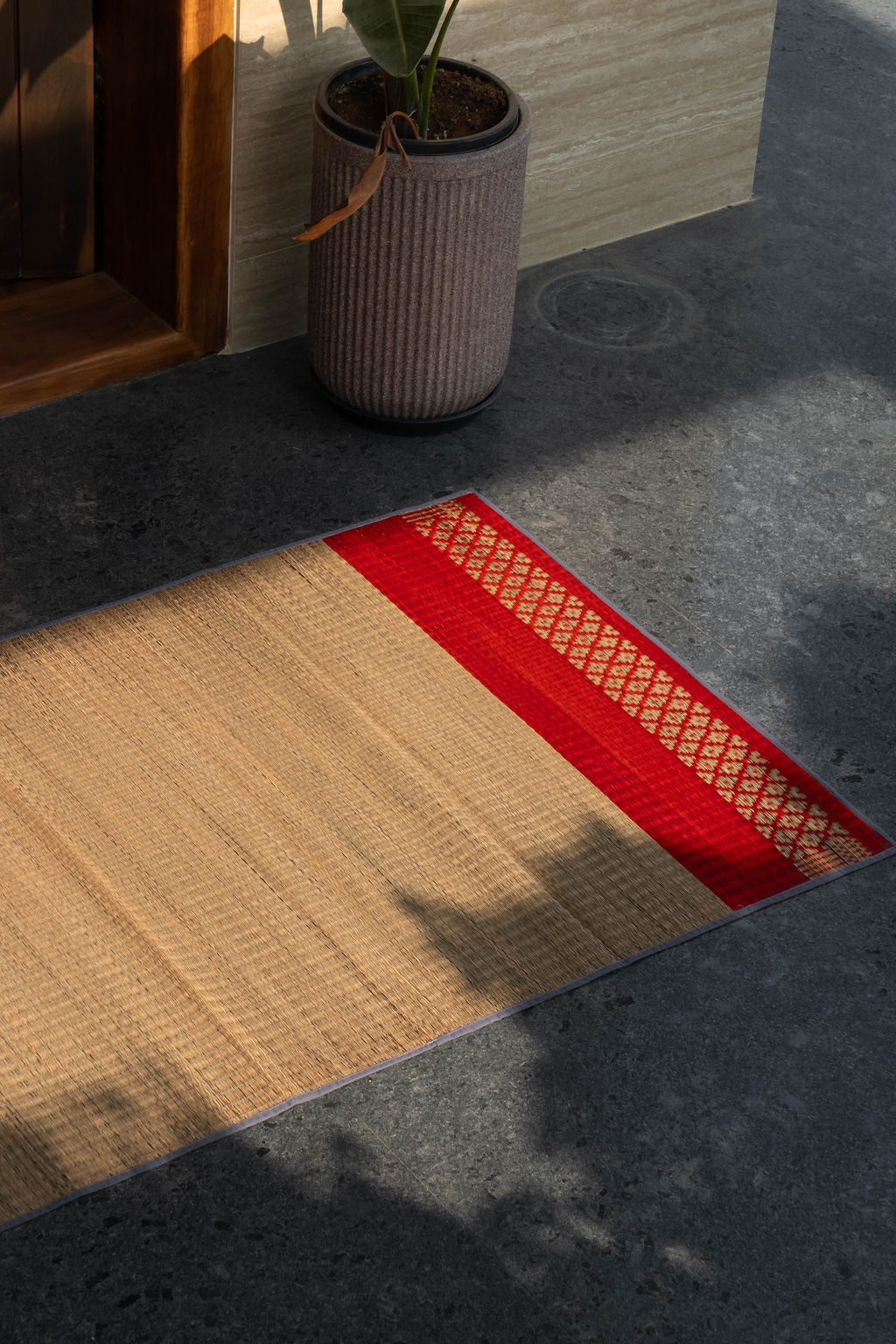 Textured grass mat with beige and red pattern on a dark floor.