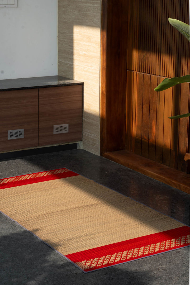 Beige rug with red border on a dark floor next to wooden furniture.