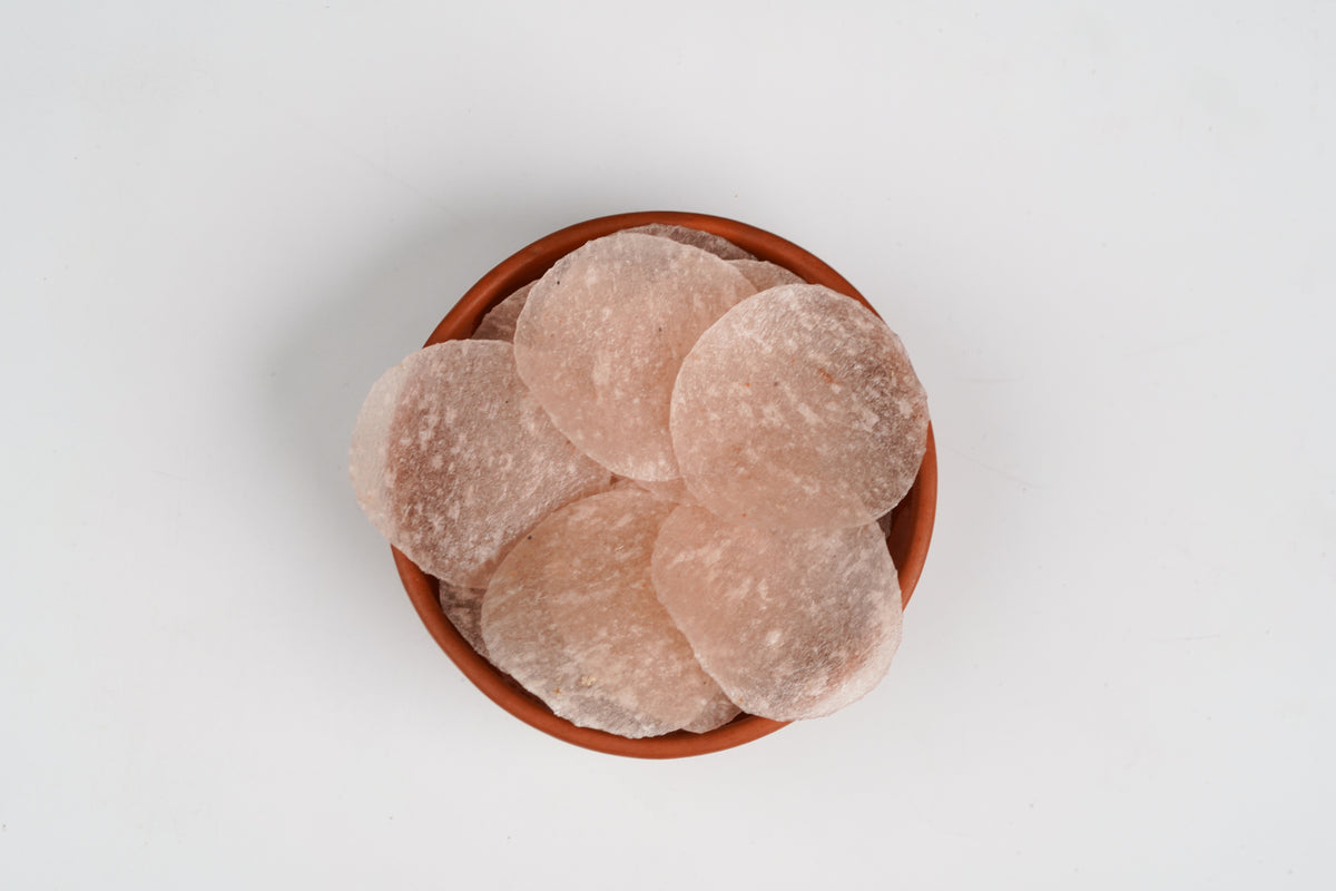Terracotta bowl filled with round, beige-colored stones on a light gray background
