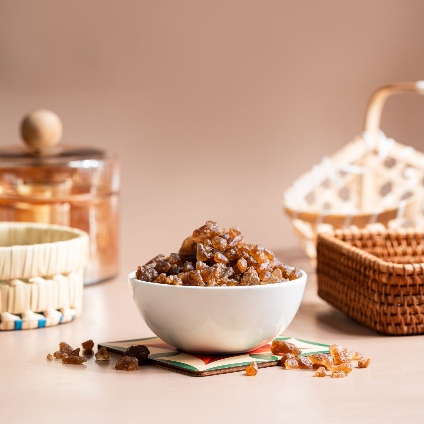 A bowl of palm candy on a table, with a basket and glass container in the background, against a beige backdrop.