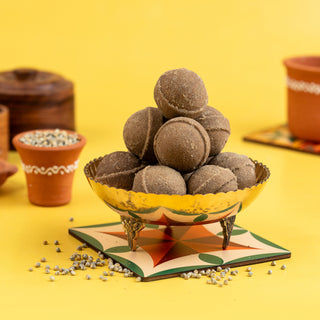 A bowl of pearl millet ghee ladoo (Kambu Ghee Ladoo) served on a decorative plate with scattered millet grains around it, against a yellow background.