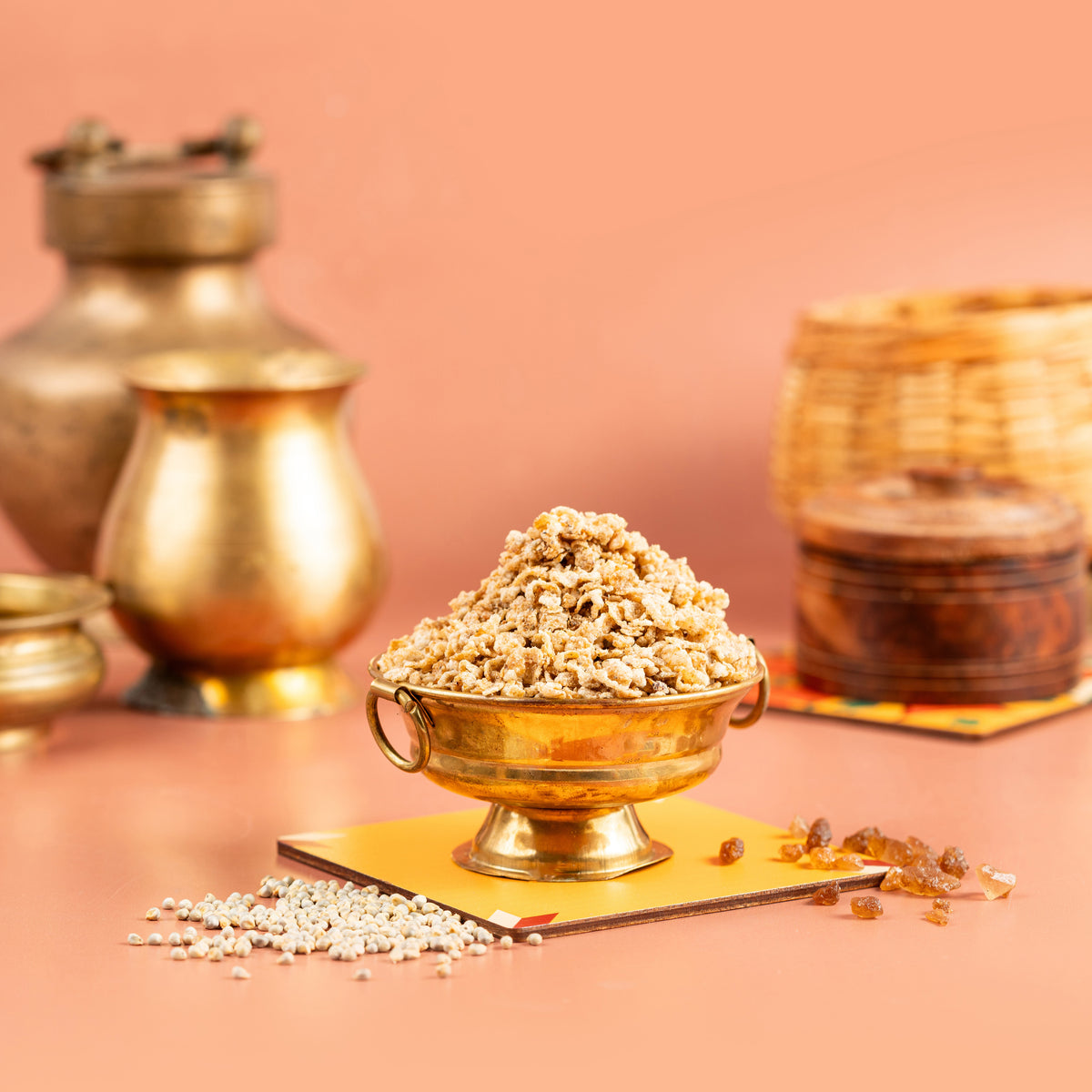 A bowl of air fried millet sweet on a yellow plate with a backdrop of traditional Indian pottery and spices.
