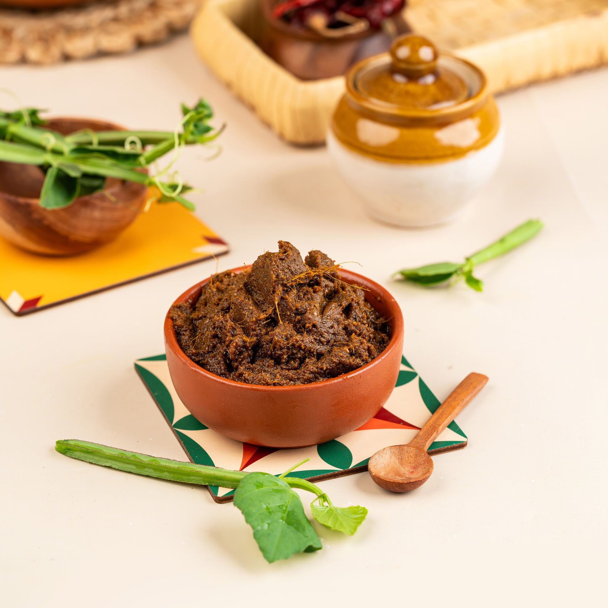 A bowl of Pirandai Thokku (a type of Sri Lankan pickle) on a colorful mat, with a spoon and green chili peppers beside it.