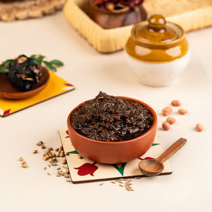 A bowl of Puliyodarai (tamarind rice) mix with spices, alongside a small bowl of tamarind pickle, on a placemat with a spoon resting on it. Background includes other food items and a jar.