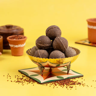 A bowl of Ragi Ghee Ladoo (Finger Millet) presented on a yellow background with a decorative border, accompanied by small cups and scattered millet grains.