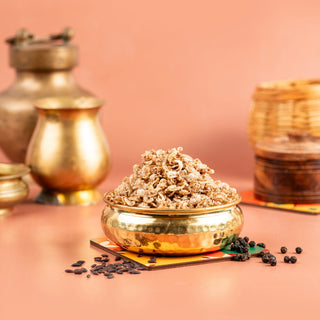 A bowl of air fried red rice spicy snack on a table with golden rice grains spilling out, against a pink background with traditional Indian pottery in the background.